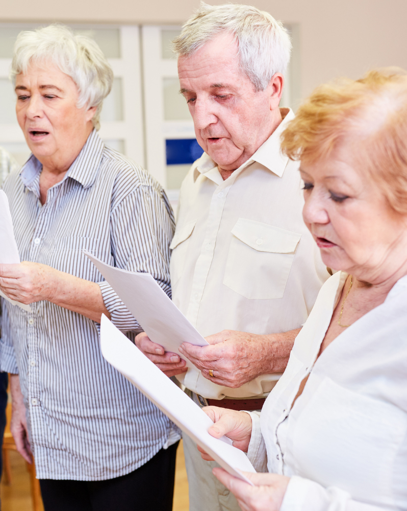 Three older people singing from a sheet